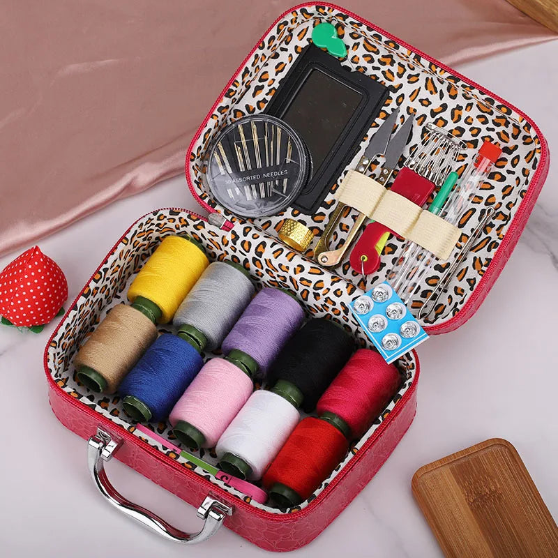 A red leather sewing kit box containing various threads, needles, and sewing tools on a pink background.