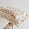A rolled floral muslin baby blanket in cream and beige tones