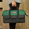 A dark green tool bag with black trim and multiple pockets is held by a person against a light wooden background.