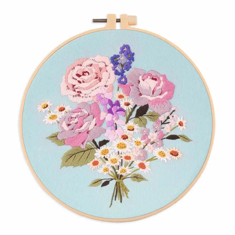 A circular embroidery hoop featuring a detailed floral design in pink, purple, and white thread on light blue fabric.