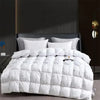 A white quilted comforter with pillows is displayed on a bed against a dark background.