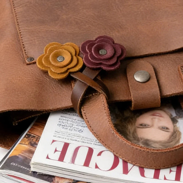 A brown leather bag features a dark purple rose charm and a leather strap.