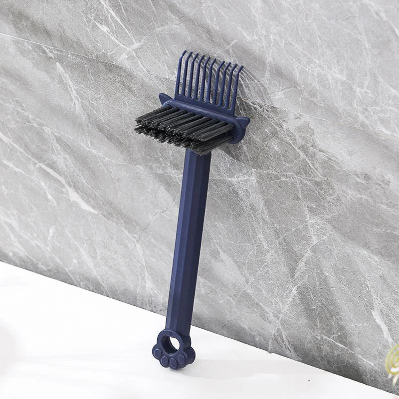 A dark blue dual-sided hairbrush cleaner with rake teeth against a gray marble background.