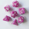 A set of seven pink and purple marbled polyhedral dice resting on a white surface.