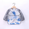 A waterproof long-sleeve baby feeding smock featuring a blue dinosaur design, displayed on a hanger.