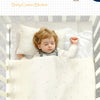 A baby is sleeping peacefully in a white soft cotton blanket on a crib mattress.
