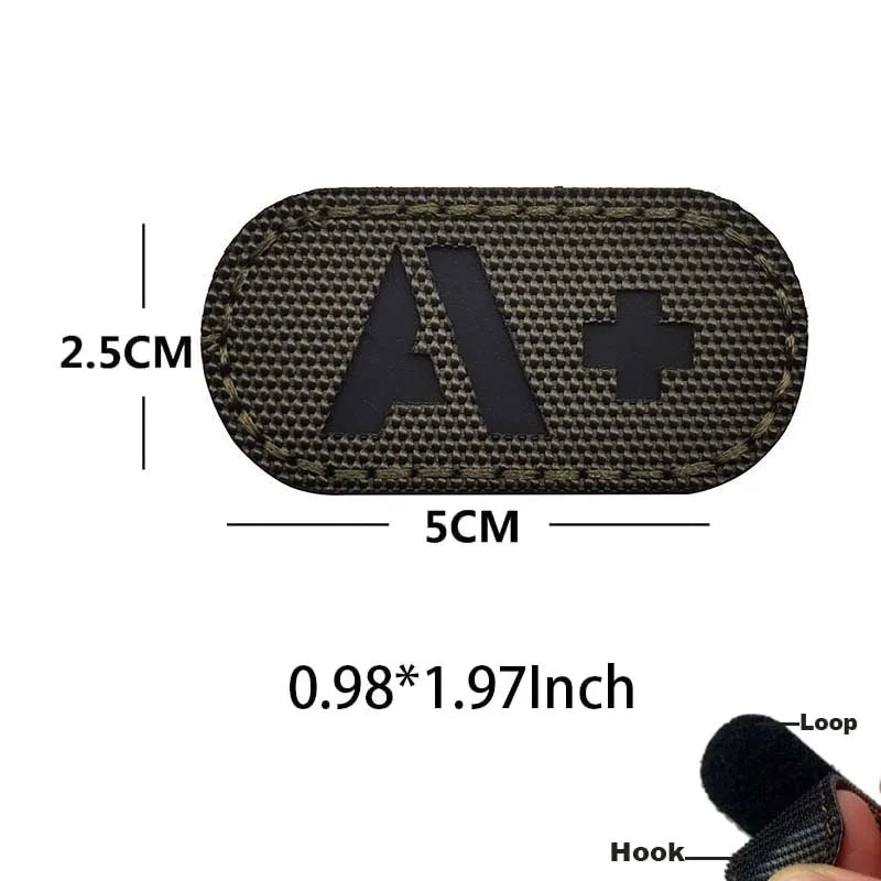 A rectangular dark tactical patch with an 'A' and a cross design, measuring 2.5cm by 5cm, with hook and loop backing.