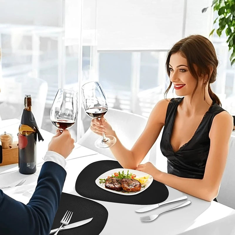 A woman is drinking red wine at a table set with black placemats and silverware.