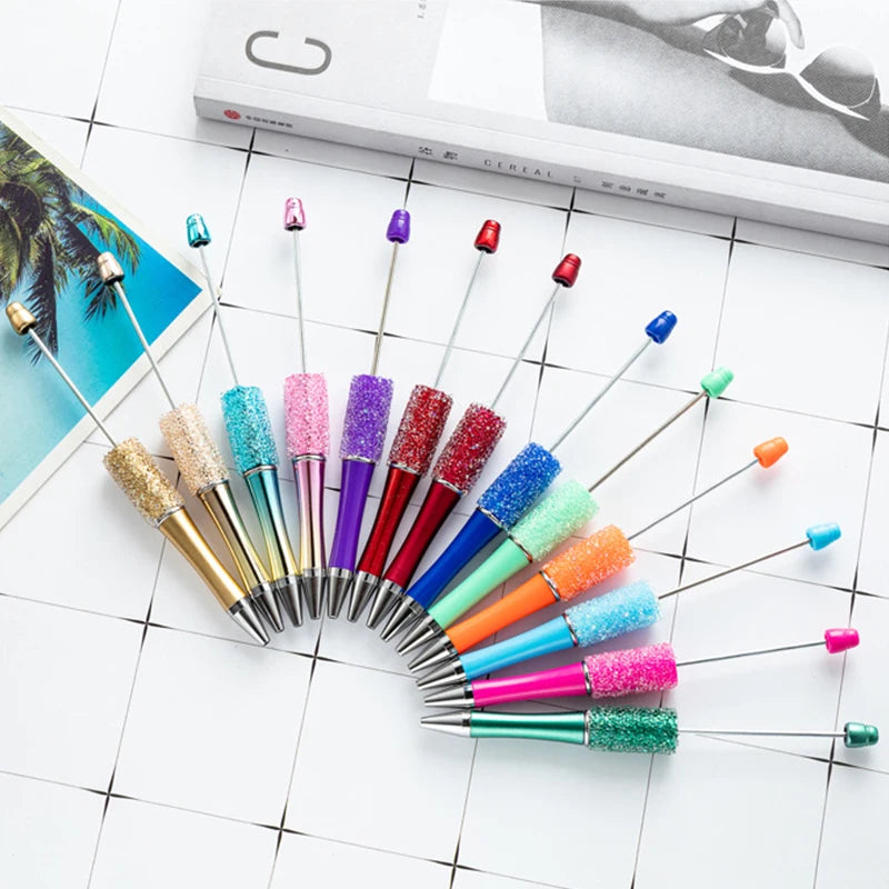 A collection of ten colorful kawaii beaded ballpoint pens arranged in a semi-circle on a white surface.