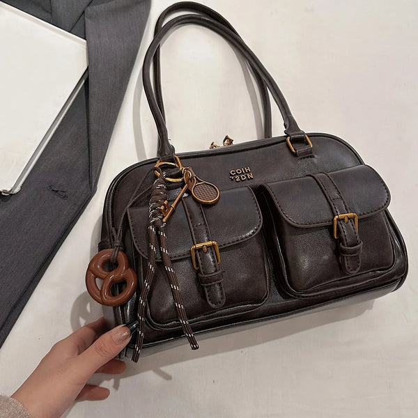 A dark brown leather multi-pocket shoulder handbag with brass hardware is being held by a hand.
