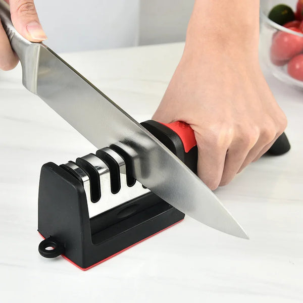A hand is using a black and red handheld knife sharpener to sharpen a stainless steel knife blade.