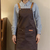 A person wearing a dark brown adjustable polyester kitchen apron over a light blue shirt.