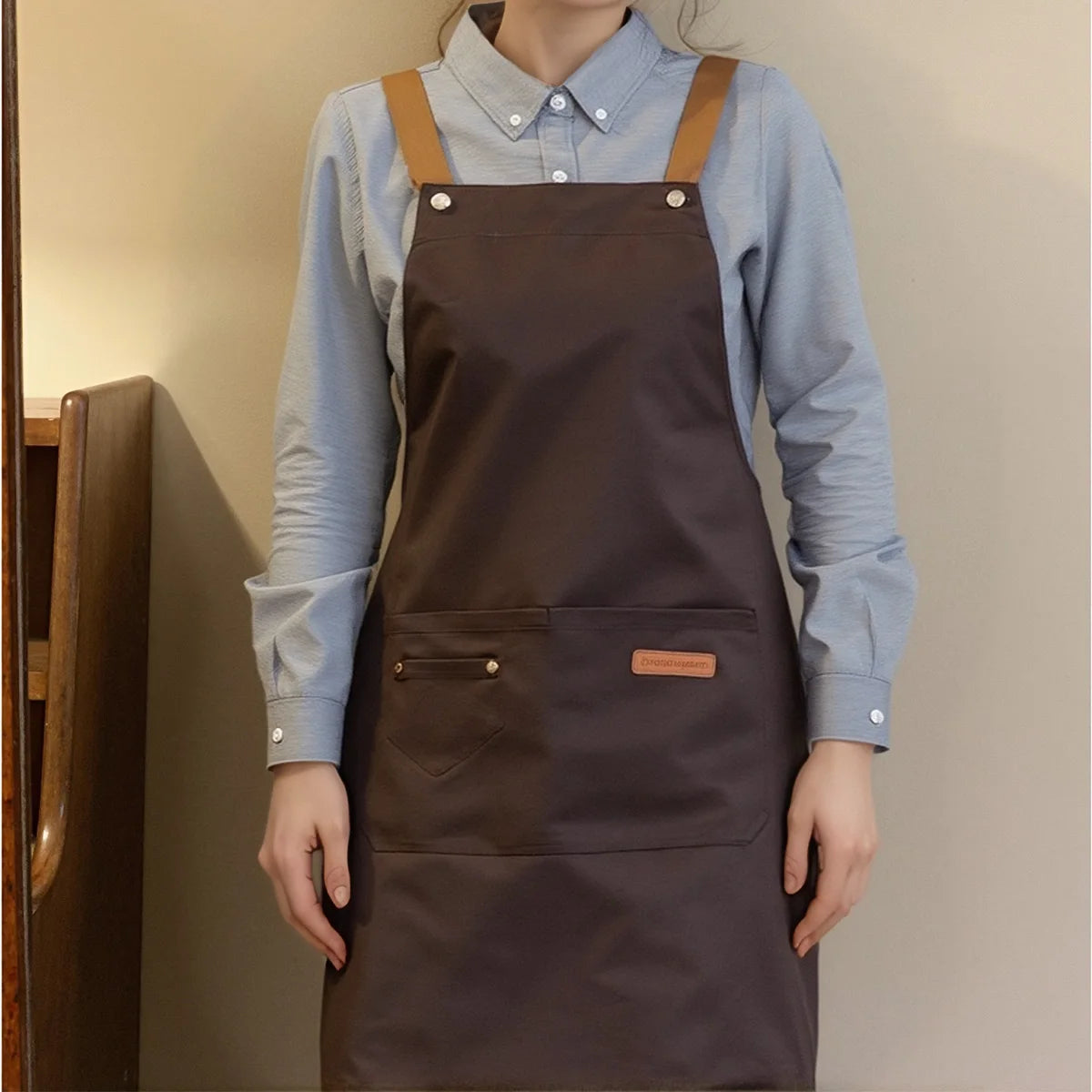 A person wearing a dark brown adjustable polyester kitchen apron over a light blue shirt.