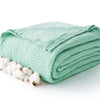 A light mint green soft muslin cotton blanket folded and accompanied by natural white cotton bolls.