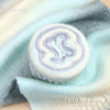 A roll of soft, colorful gradient cake yarn in white and light blue tones displayed on a light blue knitted fabric.