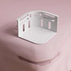 A white plastic bed sheet holder with four pink clips is shown against a soft pink background.