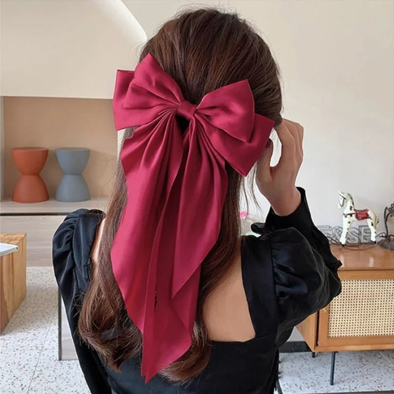 A woman shows off a deep red silk bow hair clip tied around her long brown hair.