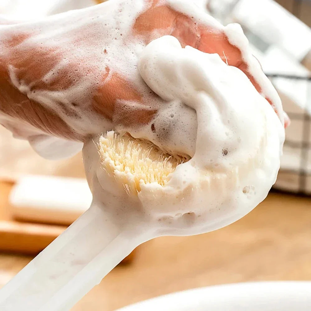 Una mano está usando un cepillo de mango largo ergonómico para aplicar espuma o crema blanca.