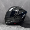 A black modular flip-up motorcycle helmet is displayed against a gray textured wall.