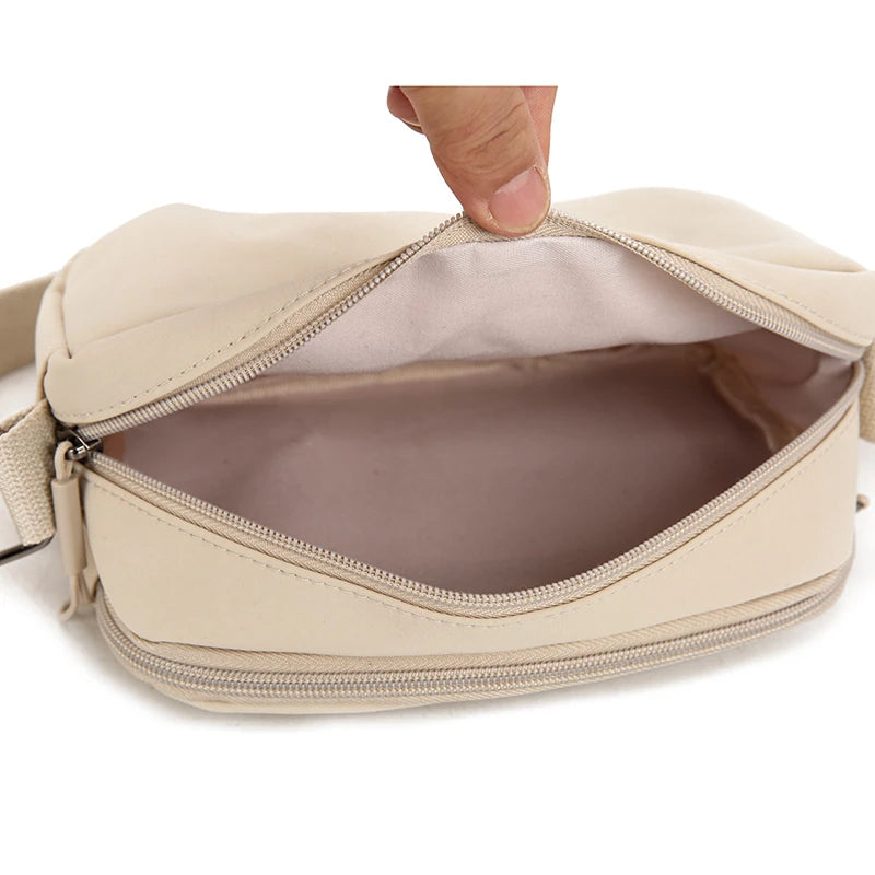 A hand opens a beige lightweight water-resistant nylon crossbody bag to show the interior pocket.