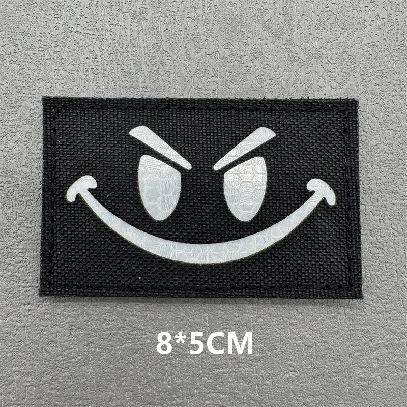 Black embroidered patch featuring a white angry face design with hook and loop backing