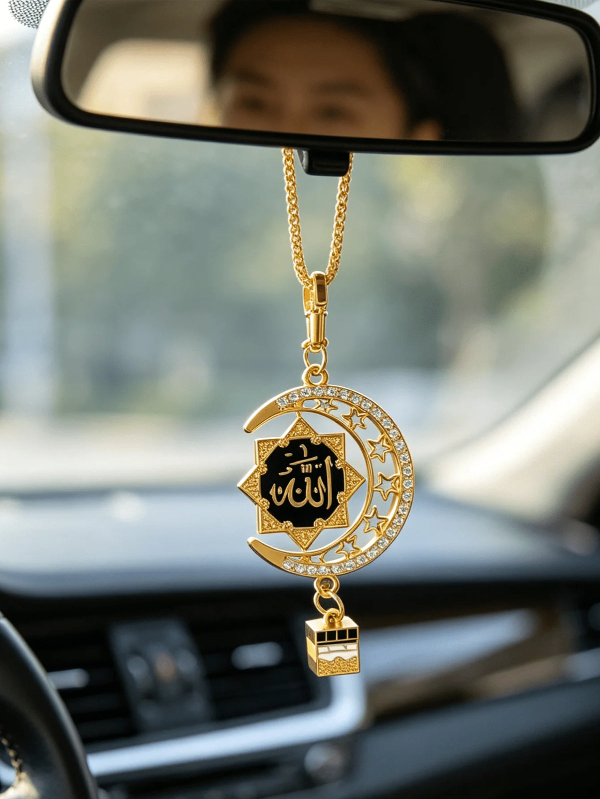 A gold-tone Islamic calligraphy pendant with a star and crescent design hanging from a chain, visible in a car mirror.
