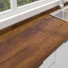 A close-up view of a dark brown wood grain countertop with a stainless steel sink and white cabinetry.