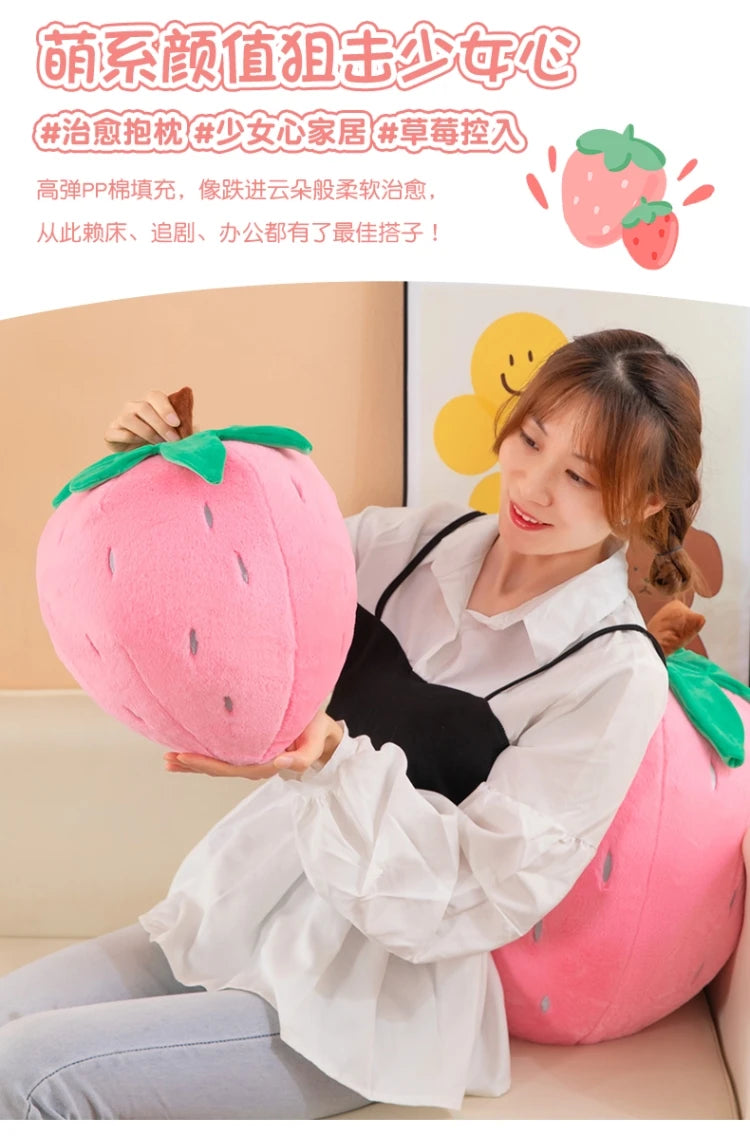 A woman is holding a pink strawberry plush throw pillow in a bright indoor setting.