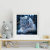 A framed print of a majestic tiger covered in sparkling blue and silver glitter, displayed next to a soft gray stuffed bear.