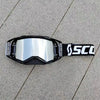 A pair of black SCOTT motocross goggles with a silver reflective lens and a black strap lying on a gray concrete surface.