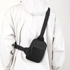 A black compact canvas crossbody sling bag worn by a person in a white hooded jacket.