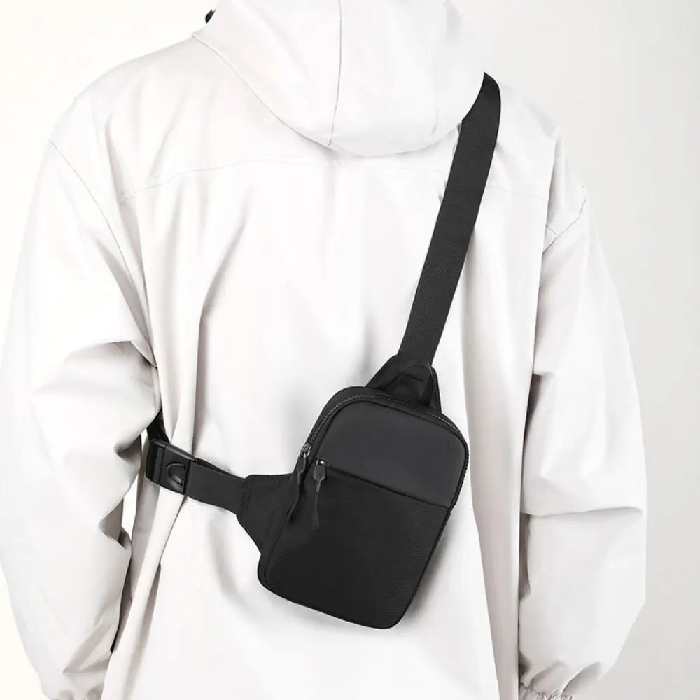 A black compact canvas crossbody sling bag worn by a person in a white hooded jacket.