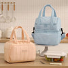 A light blue insulated lunch bag is displayed on a stand next to a pink reusable lunch bag.