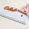 A white mechanical keyboard with pink keycaps and a wooden stand is displayed on a white fluffy surface.