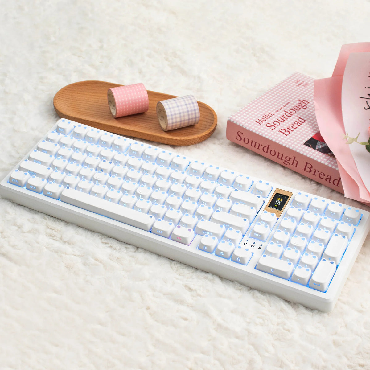 A white mechanical keyboard with pink keycaps and a wooden stand is displayed on a white fluffy surface.