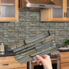A hand holds a stack of rustic gray wood tiles intended for kitchen or bathroom backsplash use.