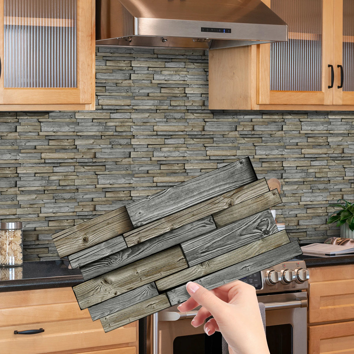 A hand holds a stack of weathered gray wood tiles intended for use as peel and stick waterproof tile stickers for a kitchen o