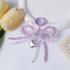 A purple pearl bow keychain with a silver heart charm displayed on a white background next to a yellow rose.