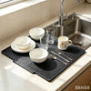 A black silicone dish drying mat with several white bowls and glasses placed on a stainless steel kitchen sink.
