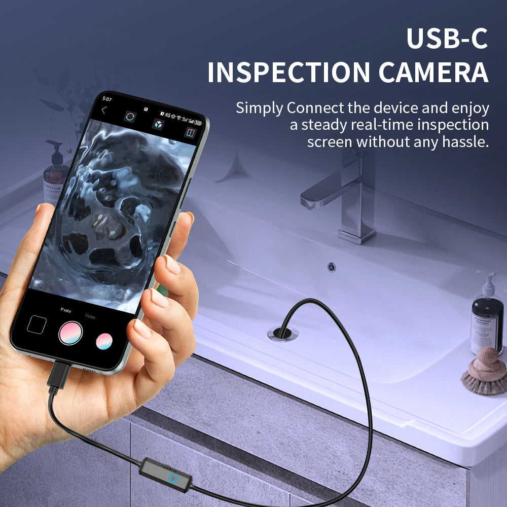 A hand holds a smartphone connected to a USB-C inspection camera, which is pointed at a bathroom fixture.