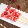 Red meat cubes skewered on bamboo sticks arranged on a white plate with chili peppers in the background.