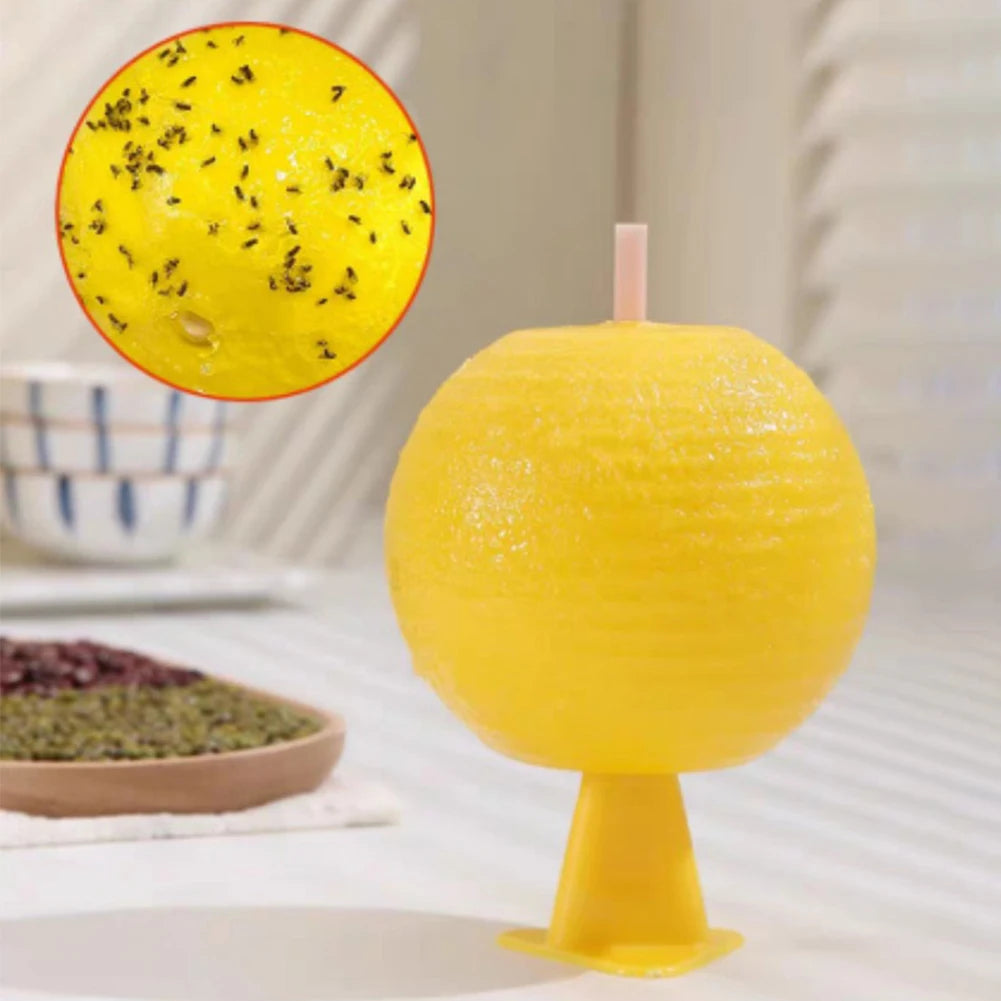 A bright yellow sticky fruit fly trap ball with a pink stick, shown next to a bowl of black seeds.