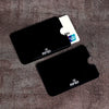A set of ten black RFID blocking card sleeves and one white card are displayed on a brown textured surface.