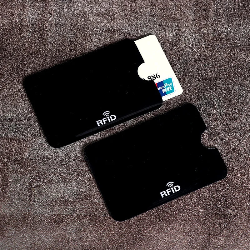 A set of ten black RFID blocking card sleeves and one white card are displayed on a brown textured surface.