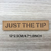 A rectangular tan woven patch with the text JUST THE TIP on a light gray wooden surface.
