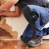 A person wearing dark t-shirt and jeans is kneeling while working, with black non-slip knee pads visible on their legs.