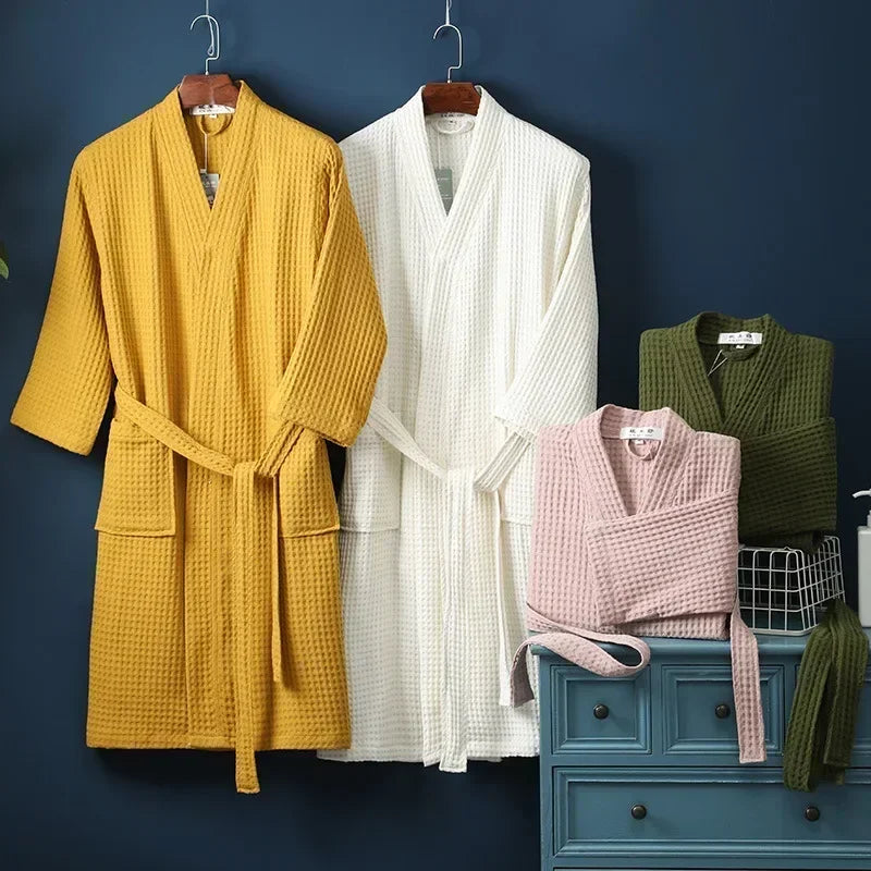 A yellow waffle knit robe and a white waffle knit robe hanging against a dark blue wall.