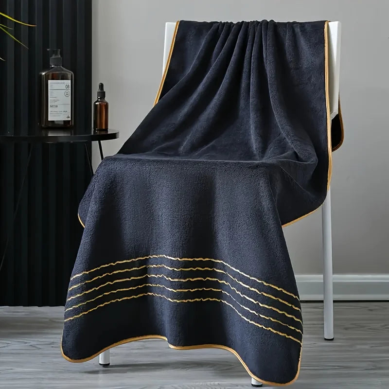 A dark gray luxury bath towel draped over a white stand with gold accents.