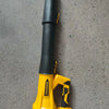 A yellow cordless leaf blower with a black handle and storage bag resting on a gray surface.