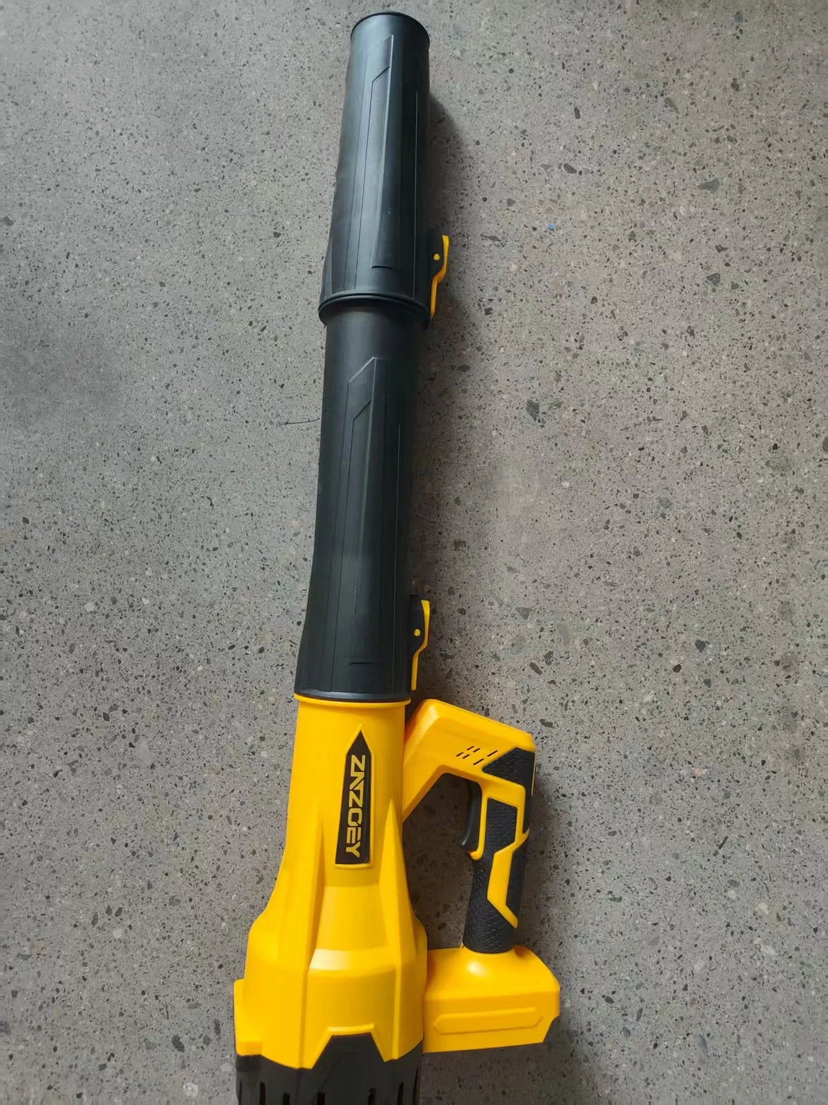 A yellow cordless leaf blower with a black handle and storage bag resting on a gray surface.